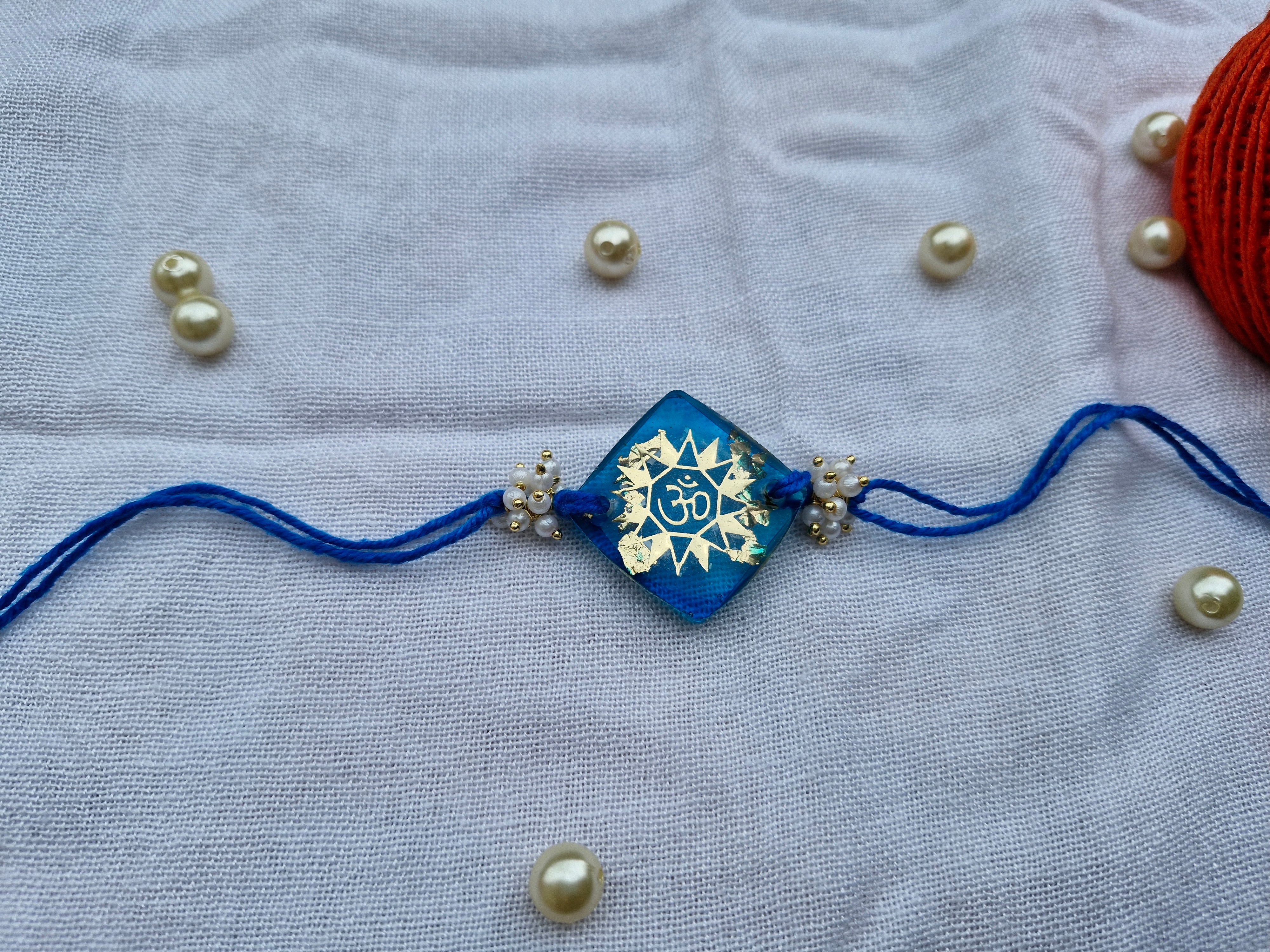 Radiant Om Rakhi – Blue Resin with Sun Motif & Pearl Beads