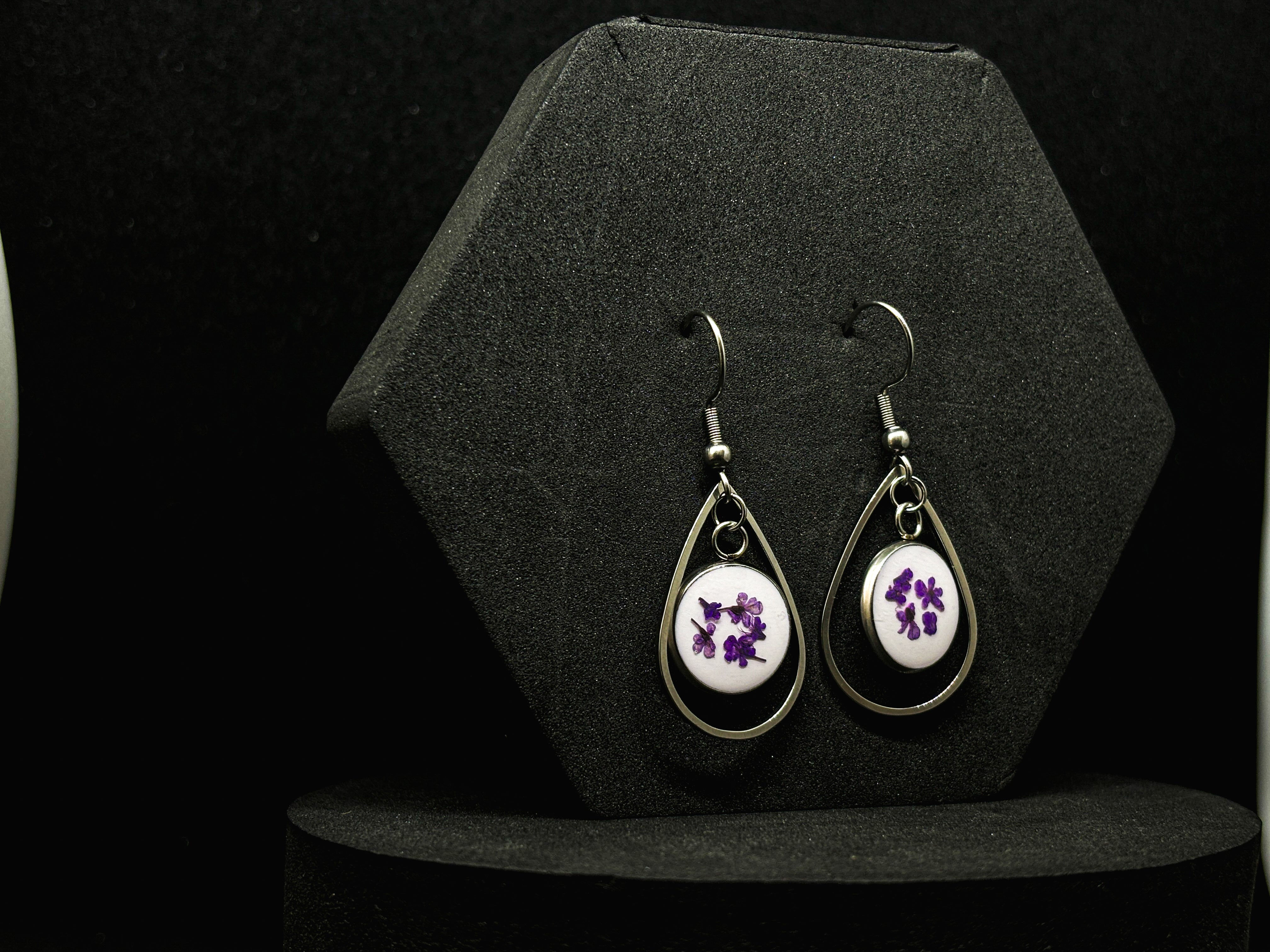 Elegant drop earrings featuring vibrant purple flowers encapsulated in clear resin within a silver-tone teardrop frame