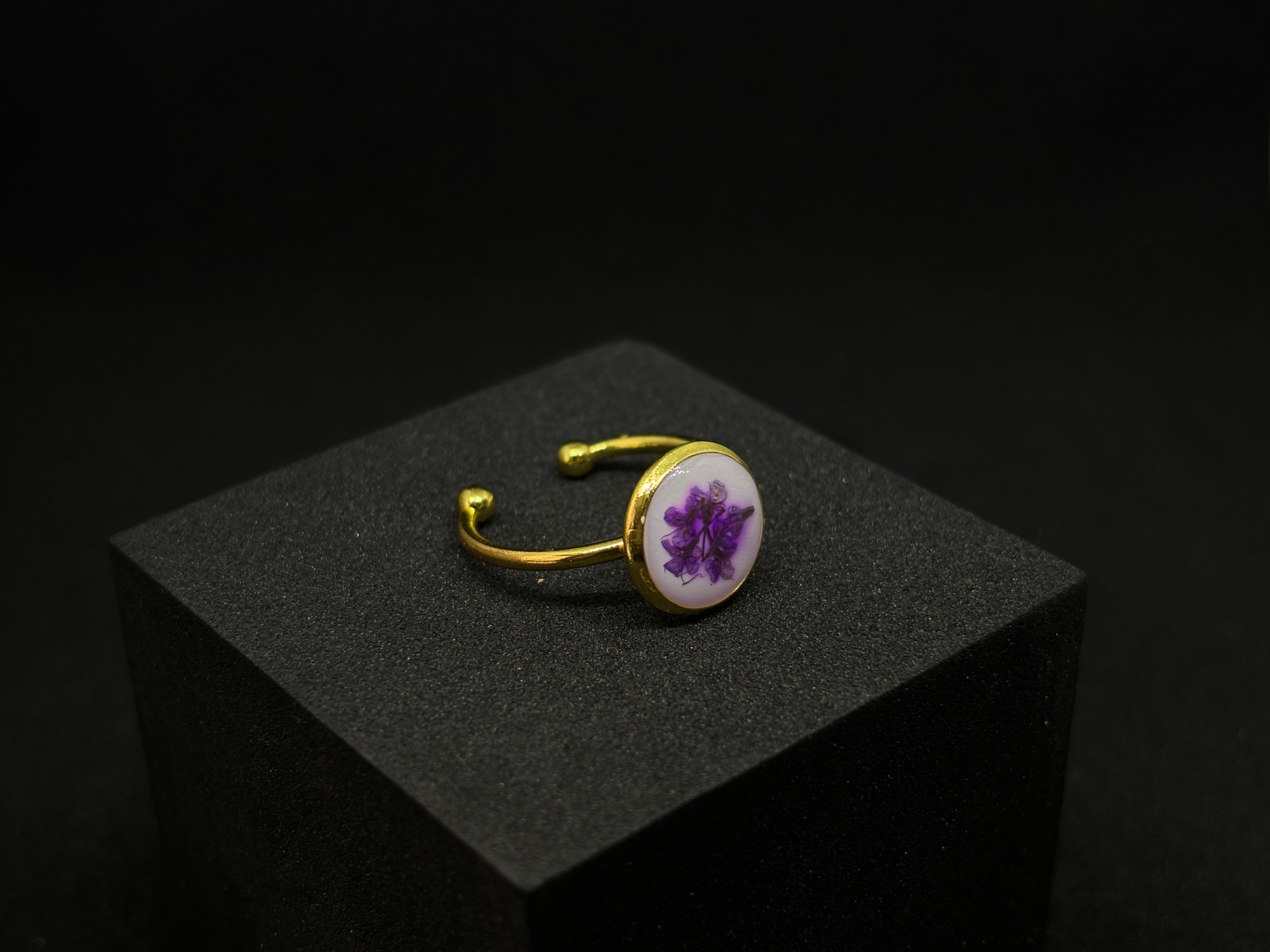 Adjustable gold-tone ring showcasing a clear resin disc with delicate purple flowers inside
